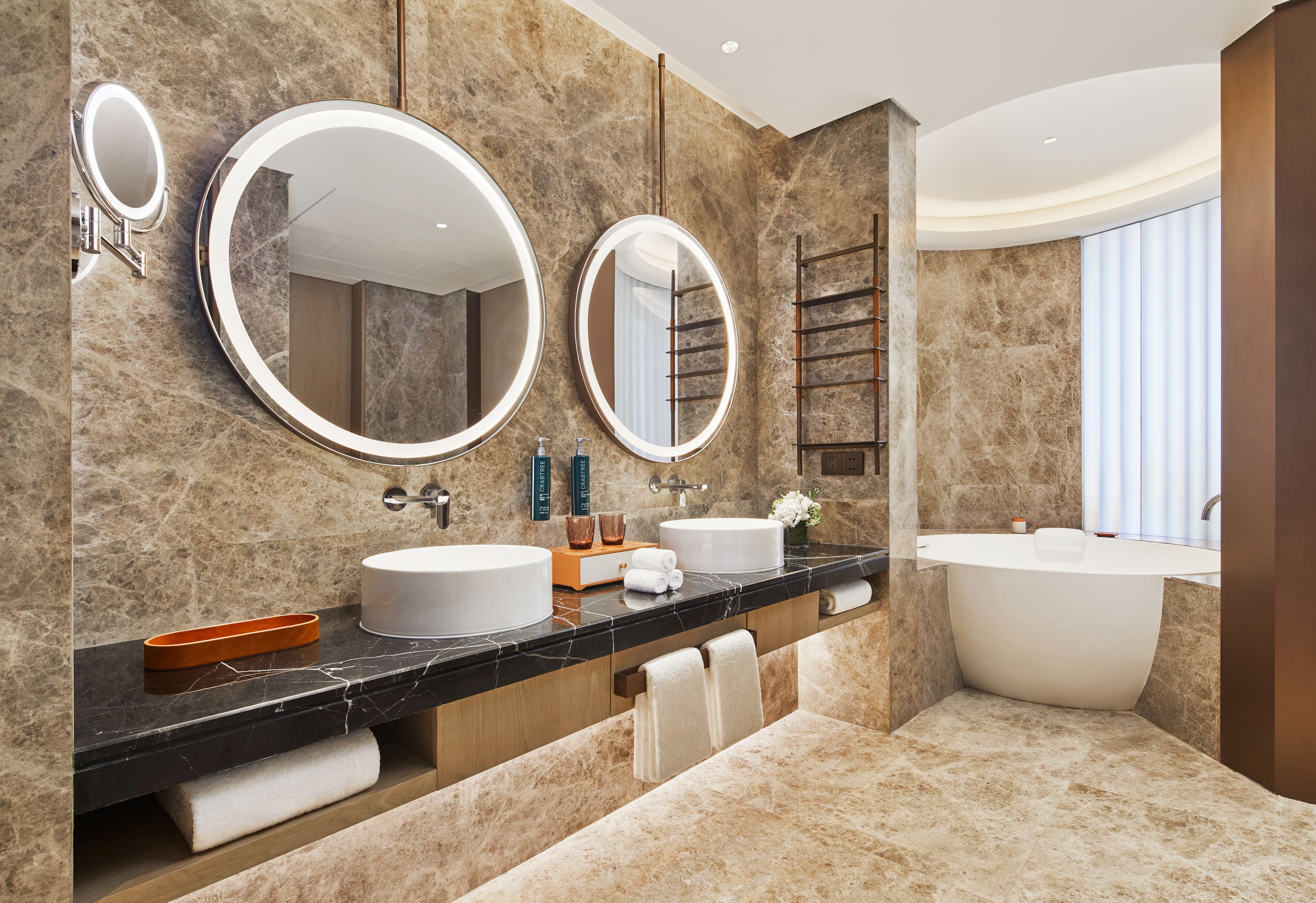 A modern bathroom with two sinks, a large bathtub, and three round mirrors.