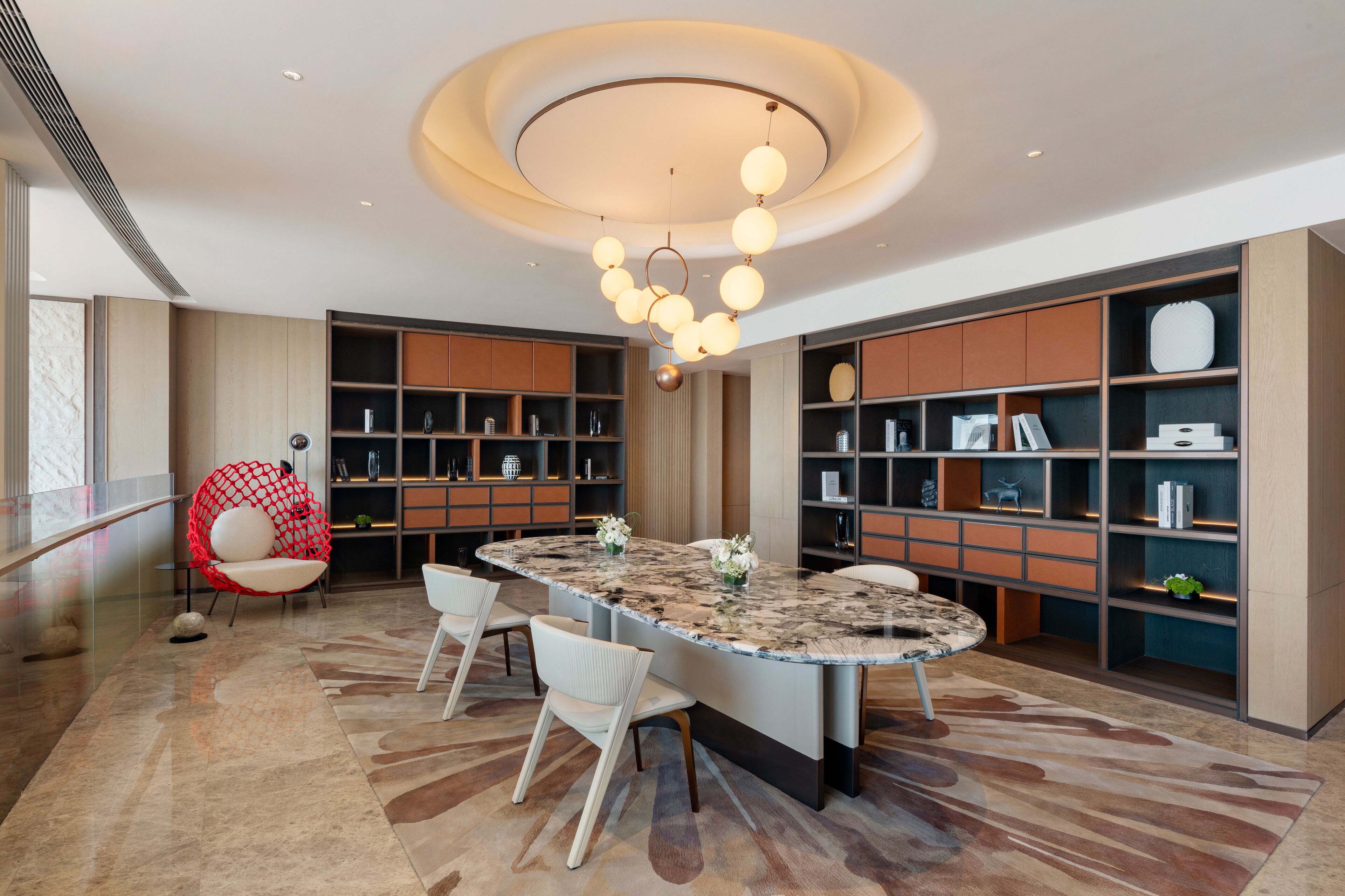A modern kitchen with a marble island, built-in shelving, and a unique red chair.