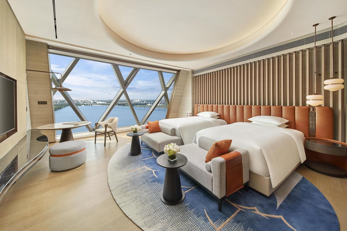 Ein modernes Hotelzimmer mit großem Fenster, einem Bett, einer Couch, einem Fernseher und einer Essecke.
