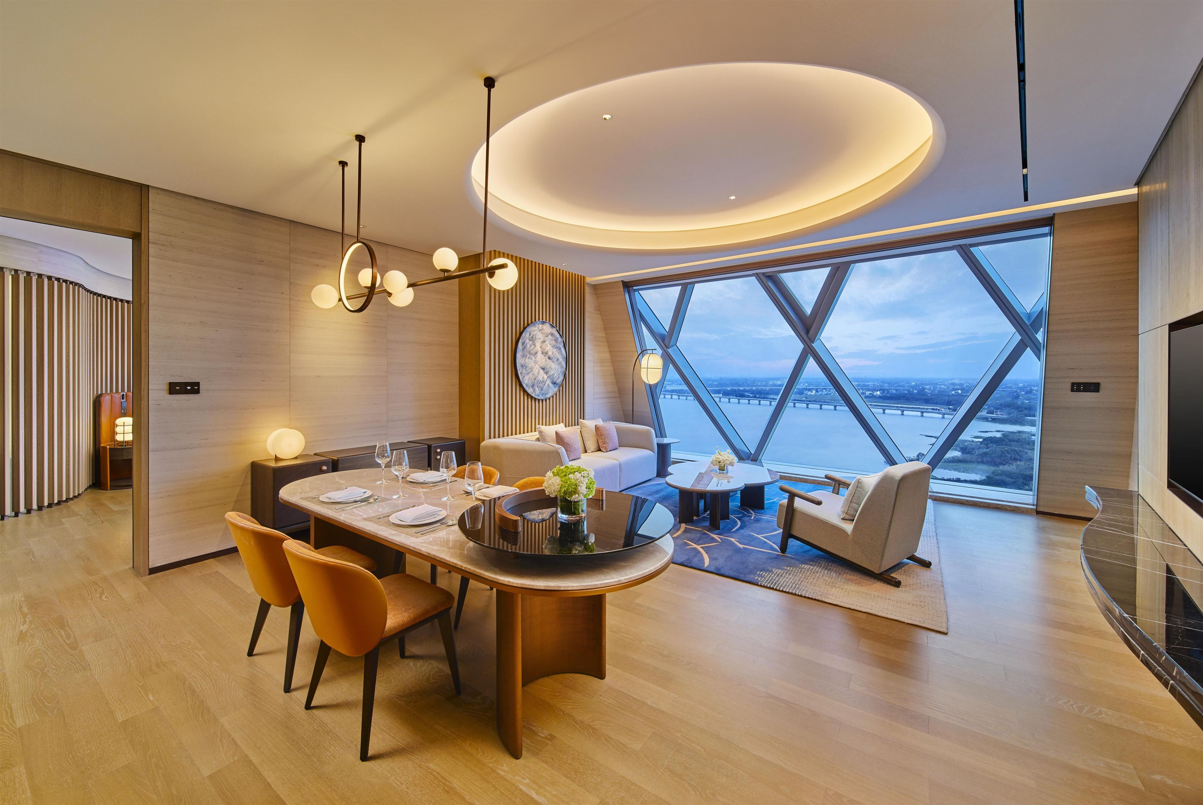 A modern dining area with a round table, chairs, and a view through large windows.