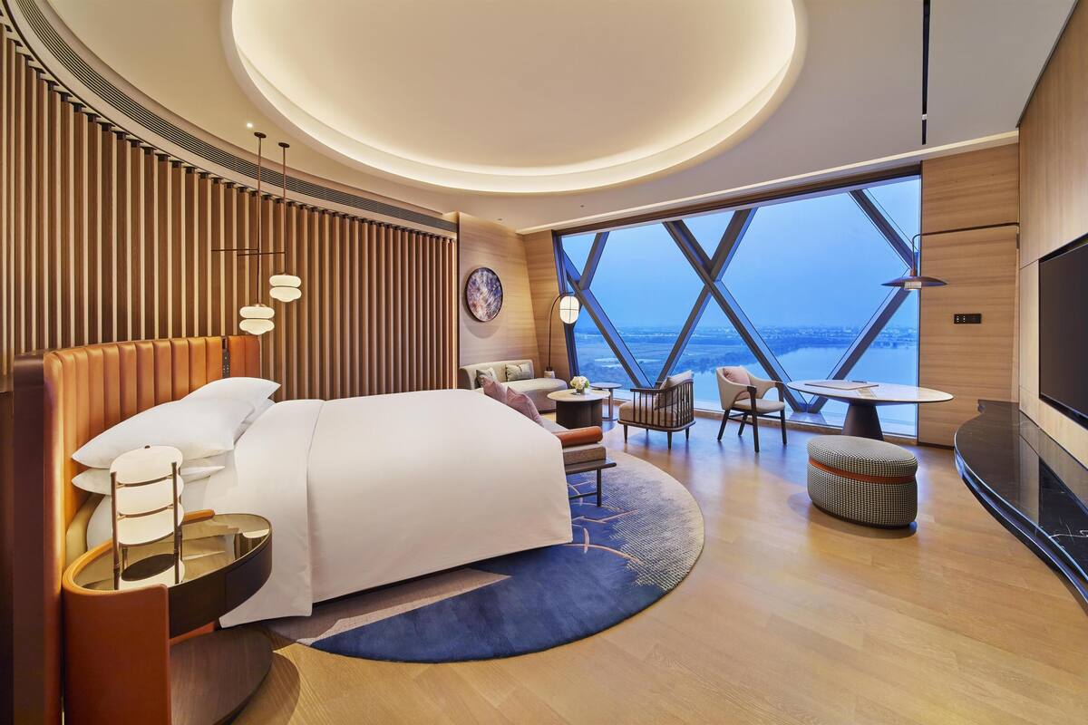 Ein modernes Hotelzimmer mit einem großen Bett, einem Fernseher, einem Essbereich und Blick auf die Stadt.