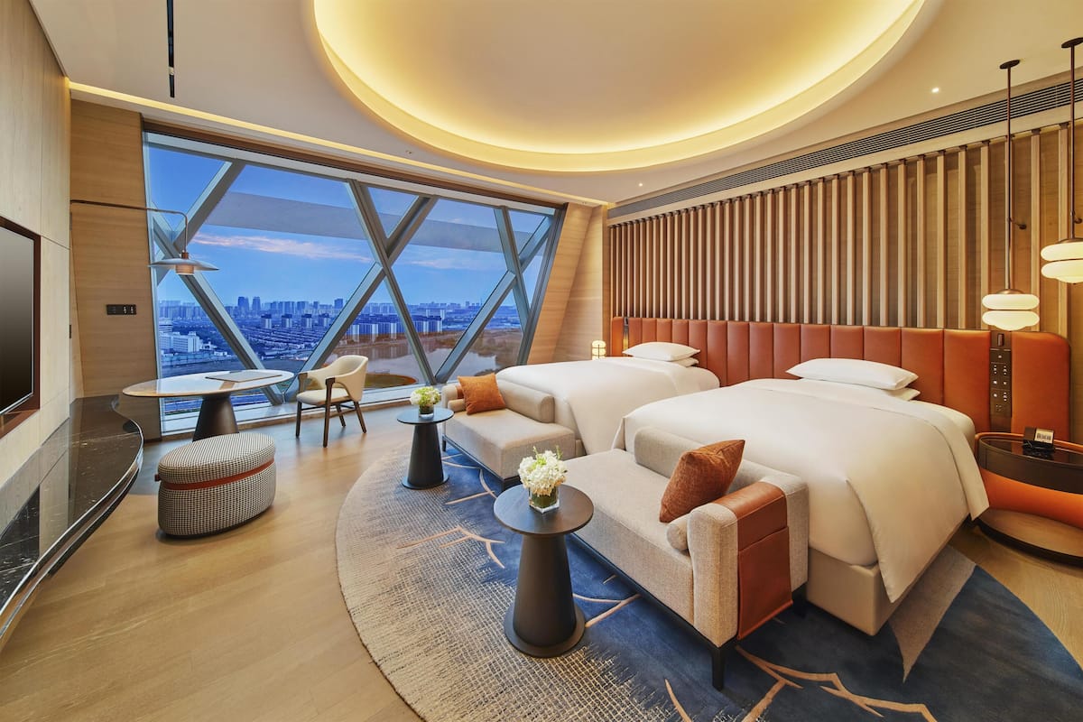Ein modernes Hotelzimmer mit großem Fenster, einem Bett, einer Couch, einem kleinen Tisch und einem Fernseher.