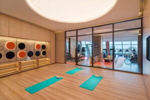 A modern gym with wooden floors, exercise mats, and a large window offering a view of the city. - Hilton Huzhou Nanxun (Huzhou)