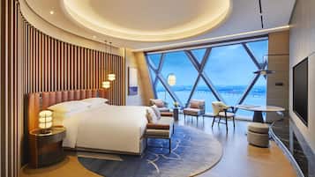 A modern hotel room with a large bed, seating area, and a view of the cityscape through large windows.