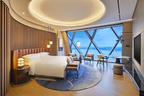 Une chambre d’hôtel moderne dotée d’un grand lit, d’un coin salon et offrant une vue sur le paysage urbain grâce à de grandes fenêtres.
