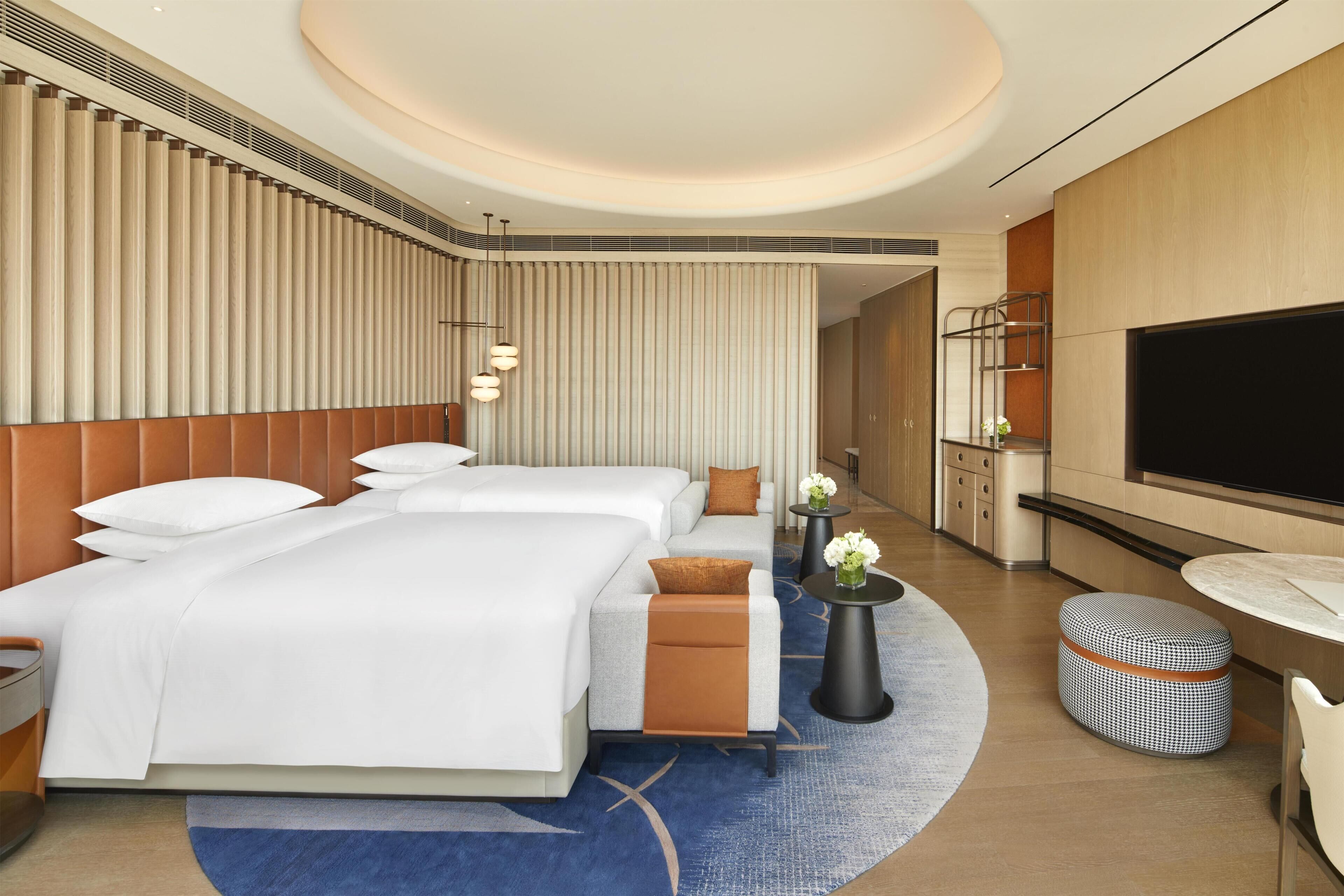 A hotel room with a large bed, a sofa, a TV, a desk, and a small table with flowers.