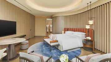 A modern hotel room with a large bed, a TV, a dining table, and a seating area.
