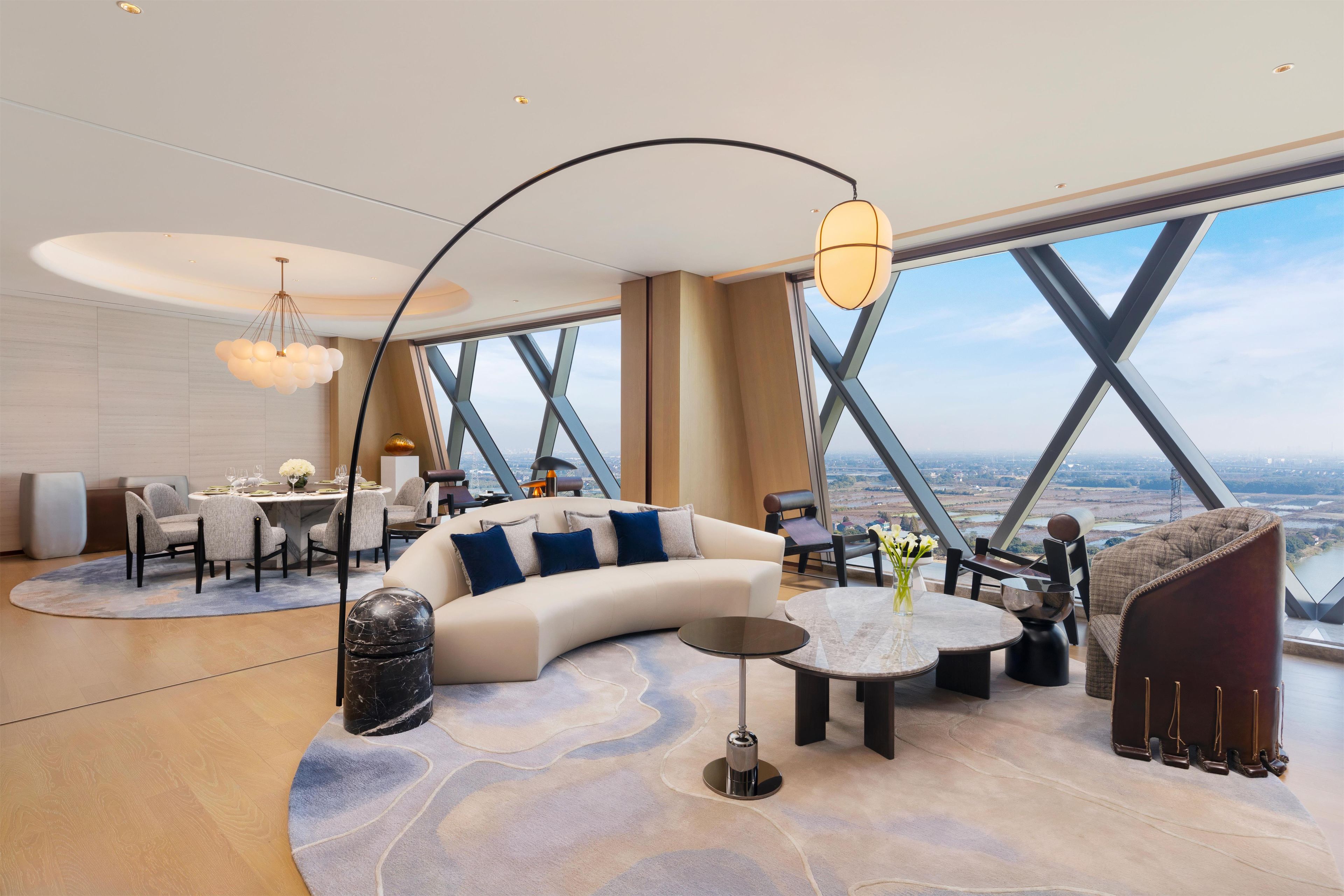 A modern interior with a curved sofa, round coffee table, and a dining area with a view.