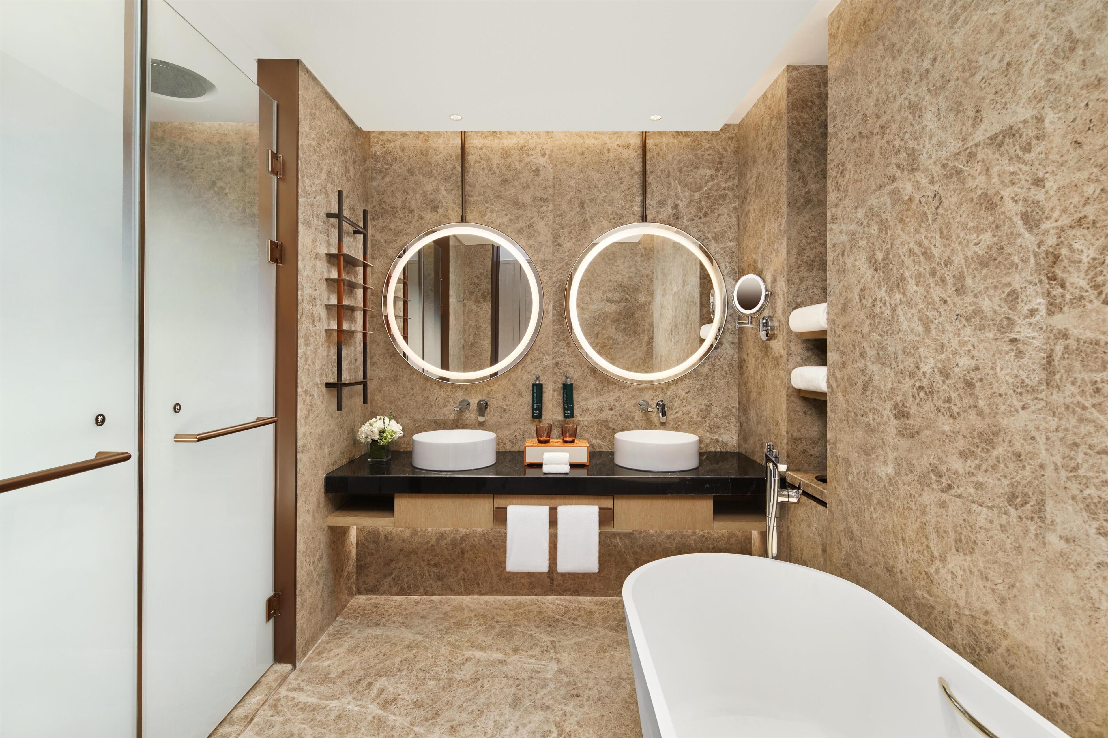 A modern bathroom with two sinks, a large mirror, a bathtub, and a glass shower enclosure.