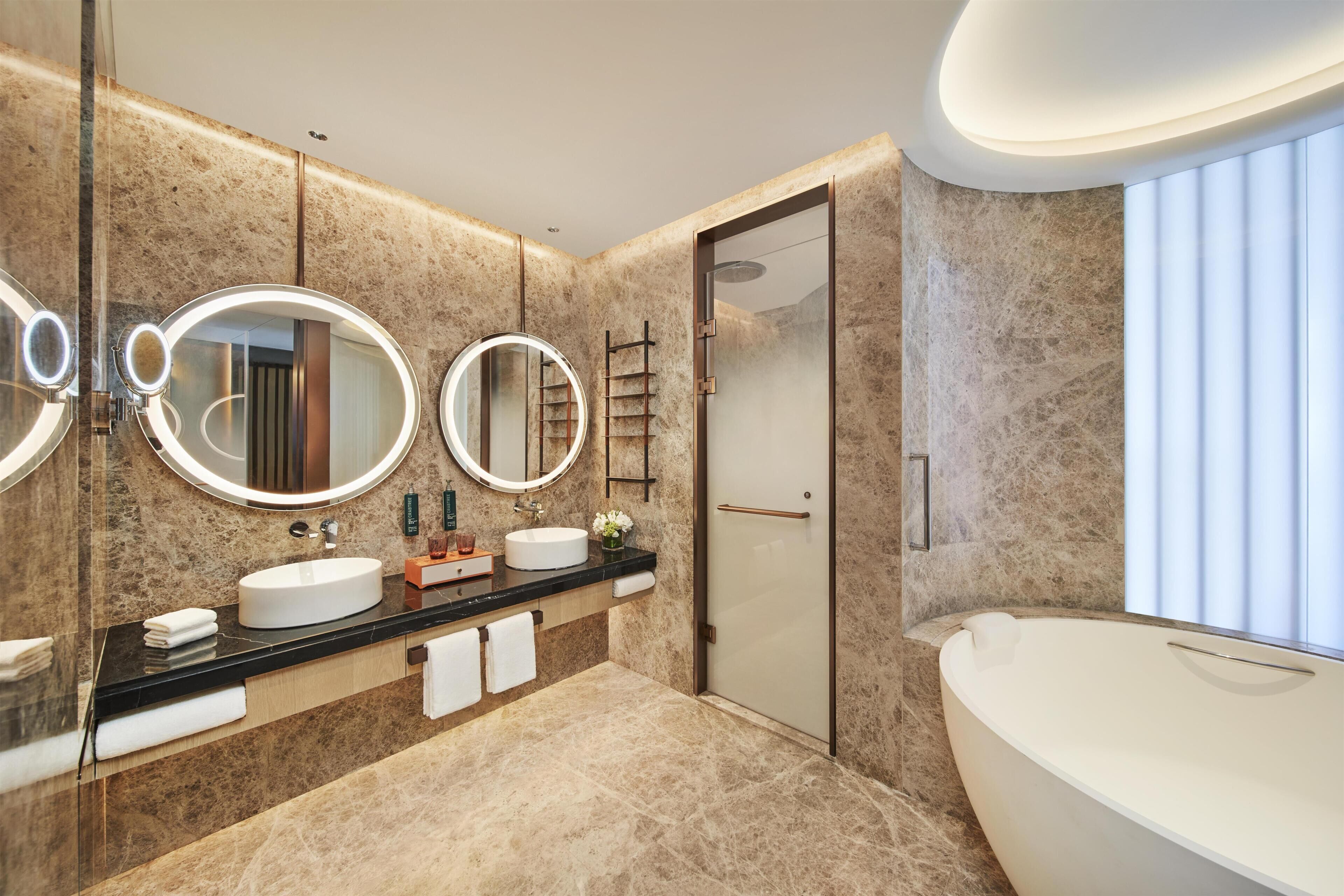 Une salle de bain moderne dotée d’une grande baignoire, d’une douche à l’italienne et d’un meuble-lavabo avec trois miroirs et un évier.