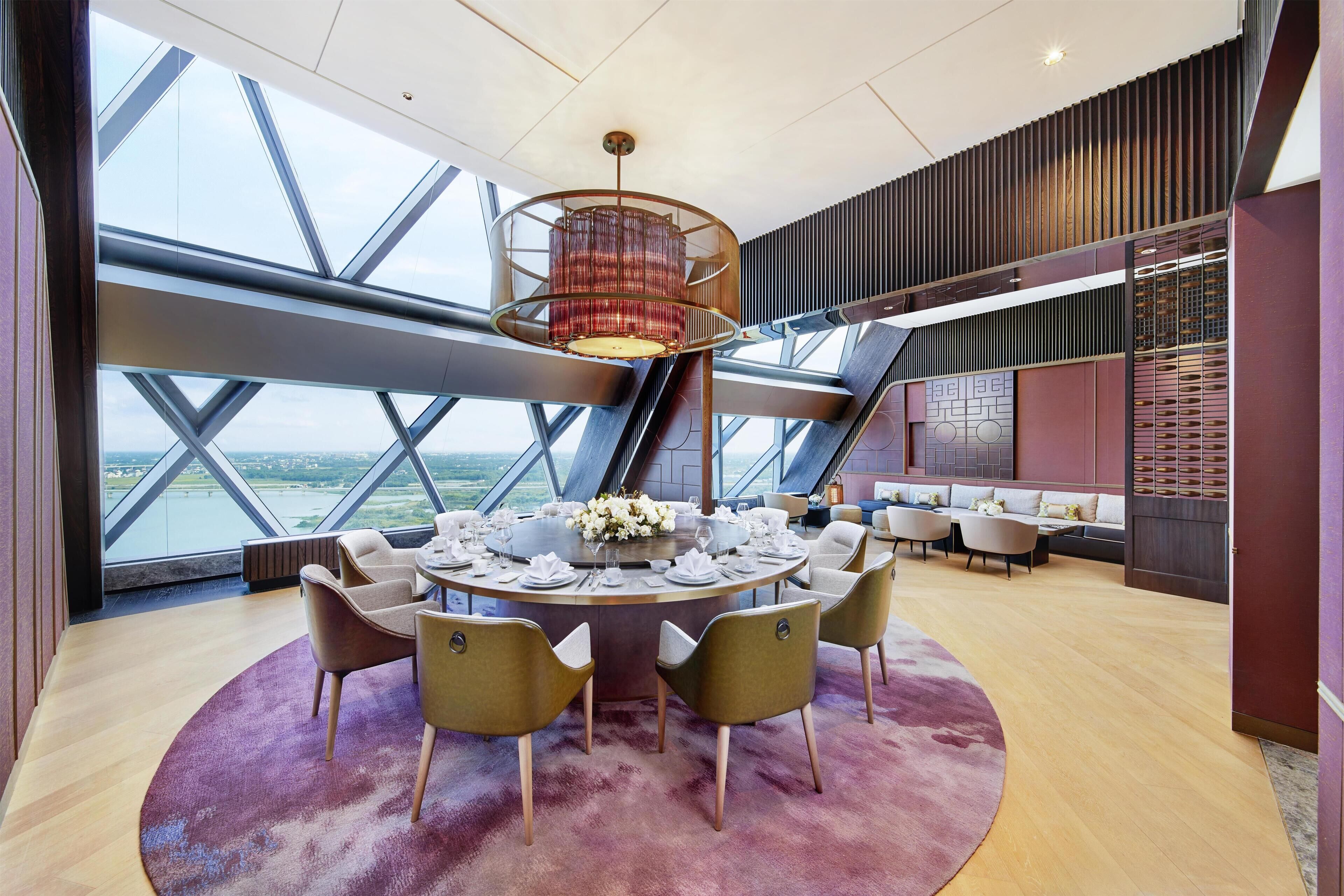 A modern dining area with a round table, chairs, and a large window offering a view of the city.