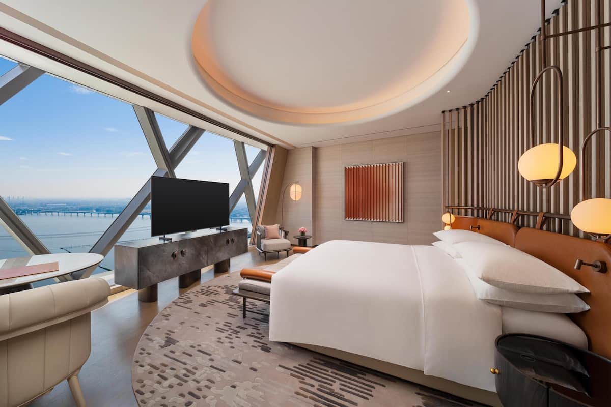 Ein modernes Hotelzimmer mit einem großen Bett, einem Fernseher, einem Schreibtisch und Blick auf die Stadt.