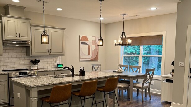 Une cuisine moderne dotée d’un îlot central, de luminaires suspendus et offrant une vue sur l’extérieur.
