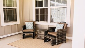 Un coin salon avec des fauteuils en osier et une petite table, situé près de grandes fenêtres à cadres blancs.