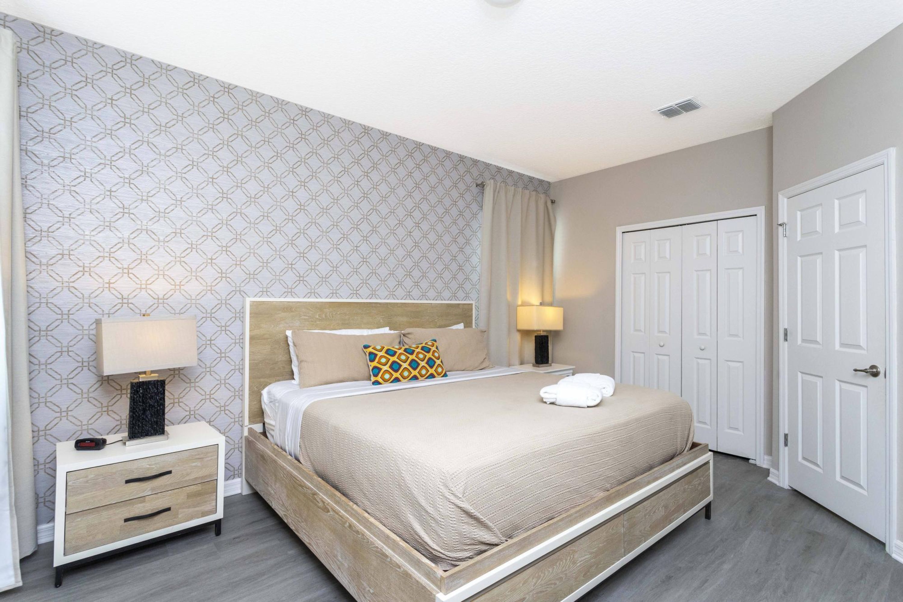 A neatly arranged bedroom with a bed, bedside tables, a wardrobe, and patterned wallpaper.