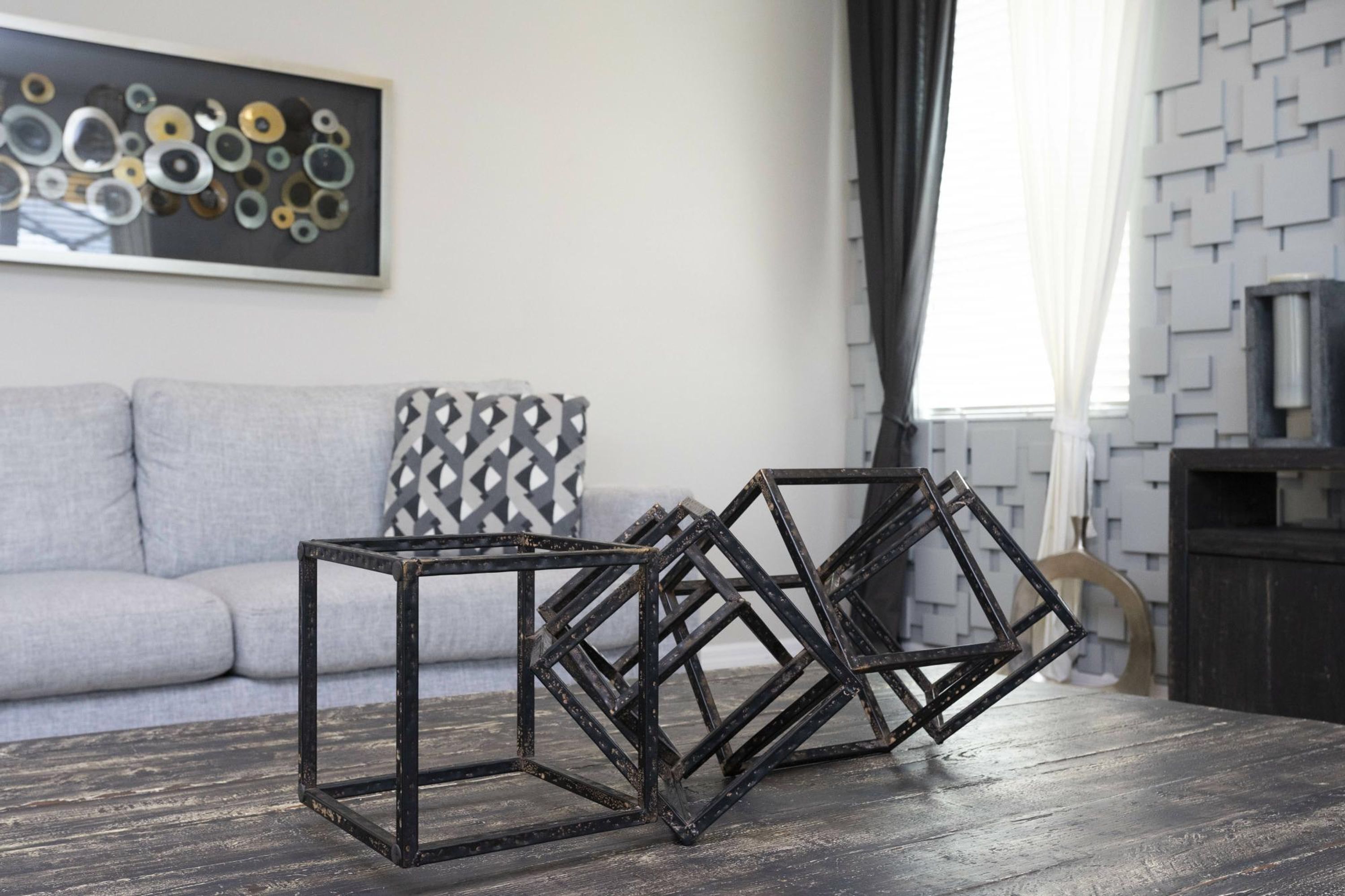 A living room with a gray sofa, a black coffee table, and a geometric wall art piece.