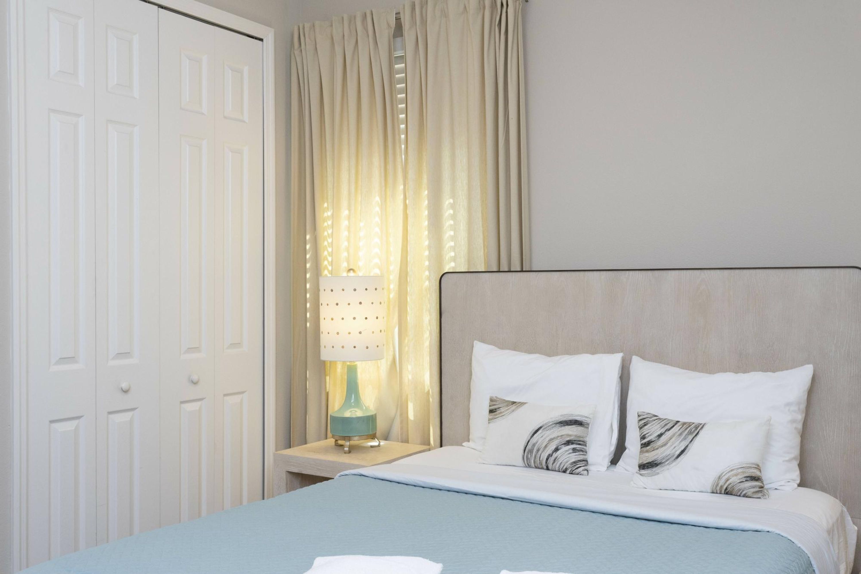 A neatly arranged hotel room with a bed, a nightstand with a lamp, and a window with curtains.