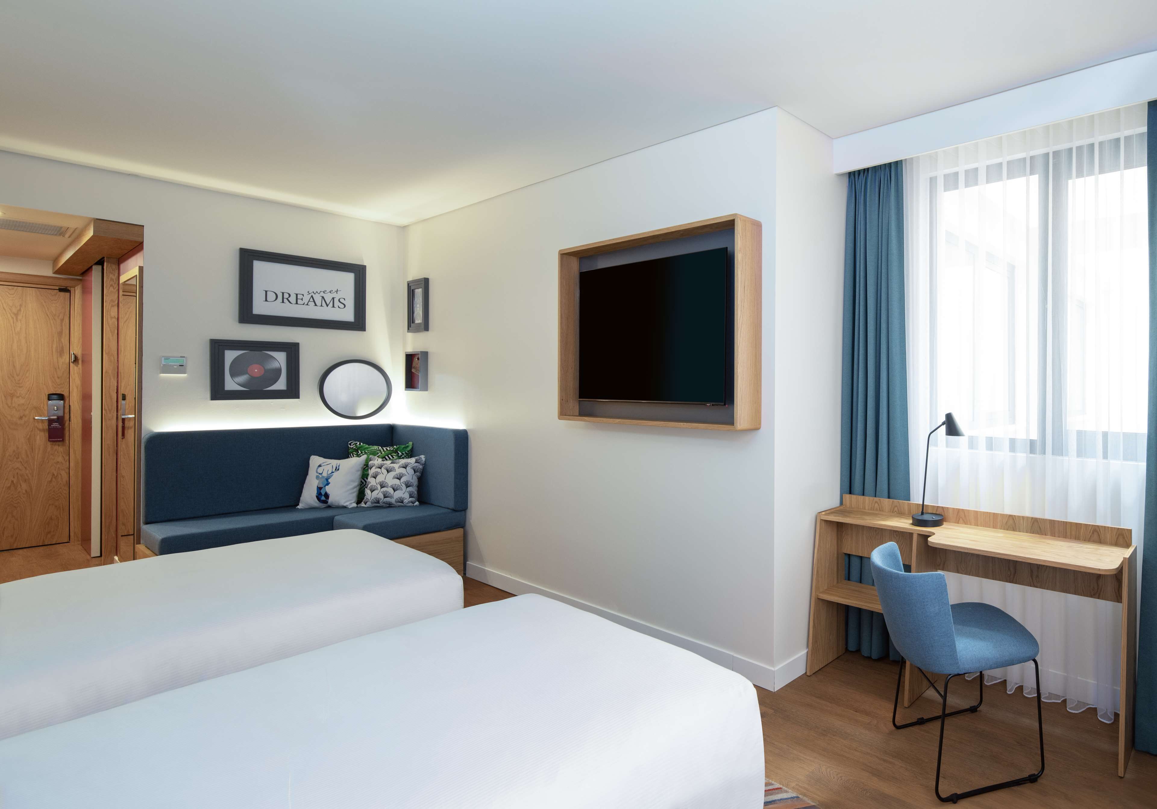 Una habitación de hotel con dos camas, un escritorio con una silla, un televisor y una ventana con cortinas.