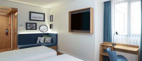 Una habitación de hotel con dos camas, un escritorio con una silla, un televisor y una ventana con cortinas.