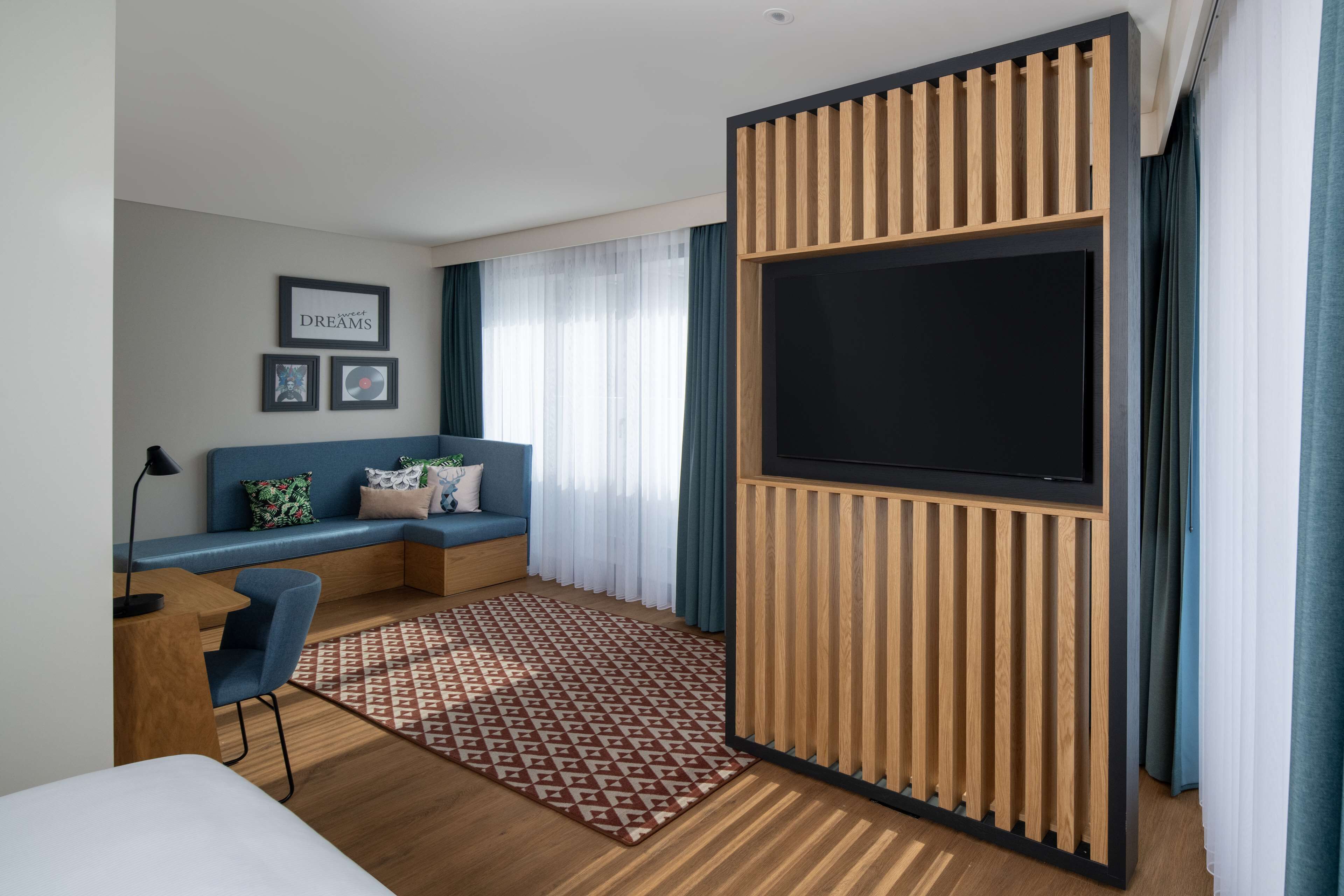 Ett modernt hotellrum med en stor TV, en soffa, ett skrivbord och en mönstrad matta.