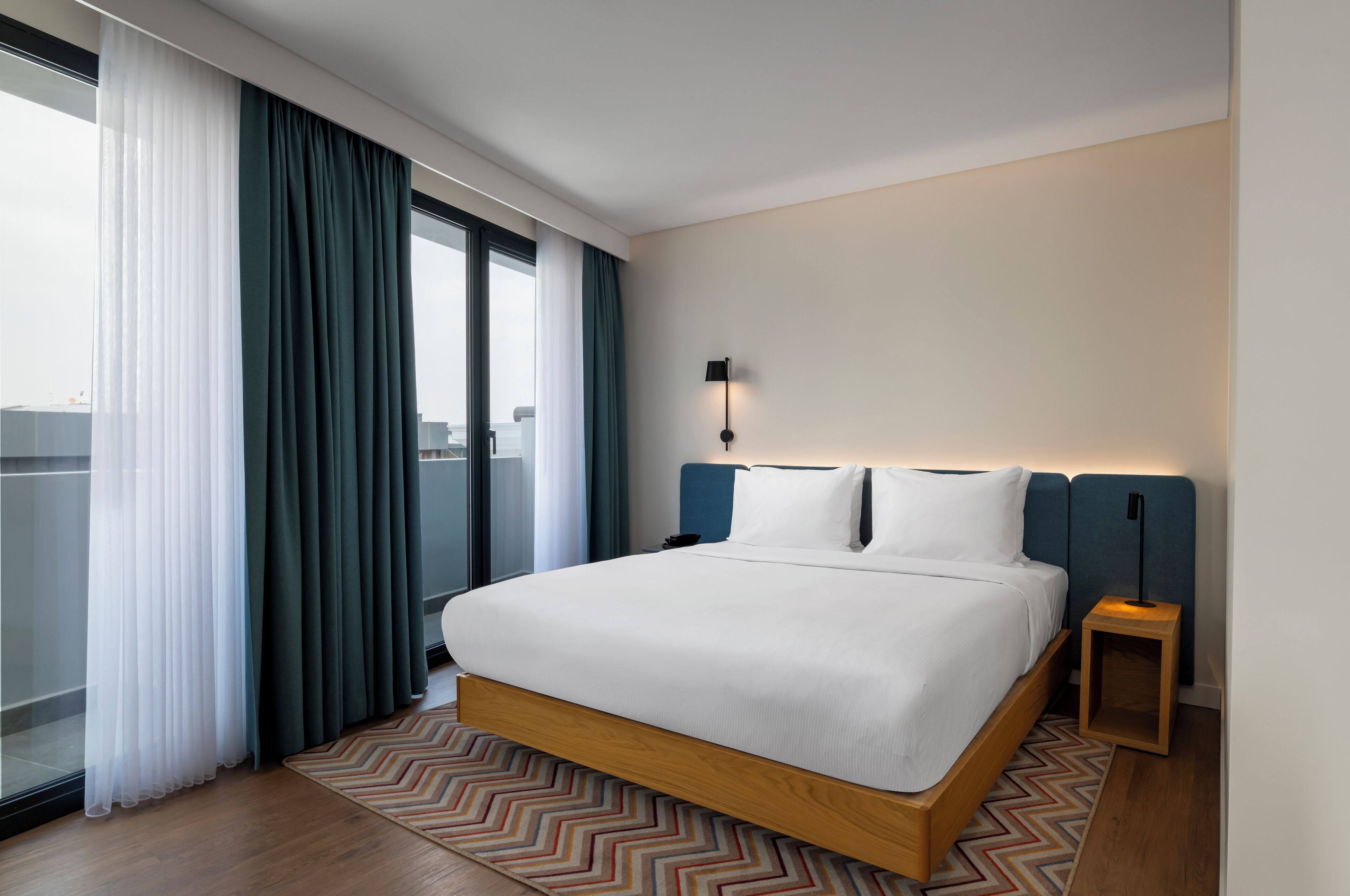 Une chambre d’hôtel moderne avec un grand lit, une vue sur la ville et une petite table de chevet.