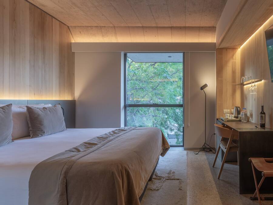 A modern bedroom with a large bed, a desk, and a view of trees through a window.