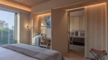 A modern bedroom with a large bed, a desk with a chair, a wardrobe, and a bathroom visible through an open door.