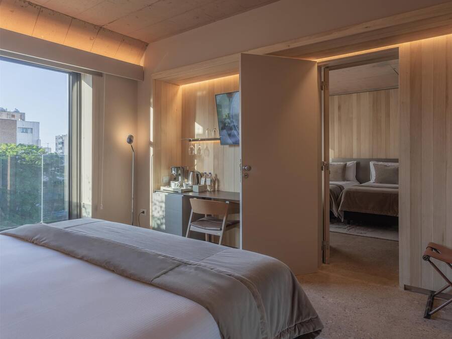 A modern bedroom with a large bed, a desk with a chair, a wardrobe, and a bathroom visible through an open door.
