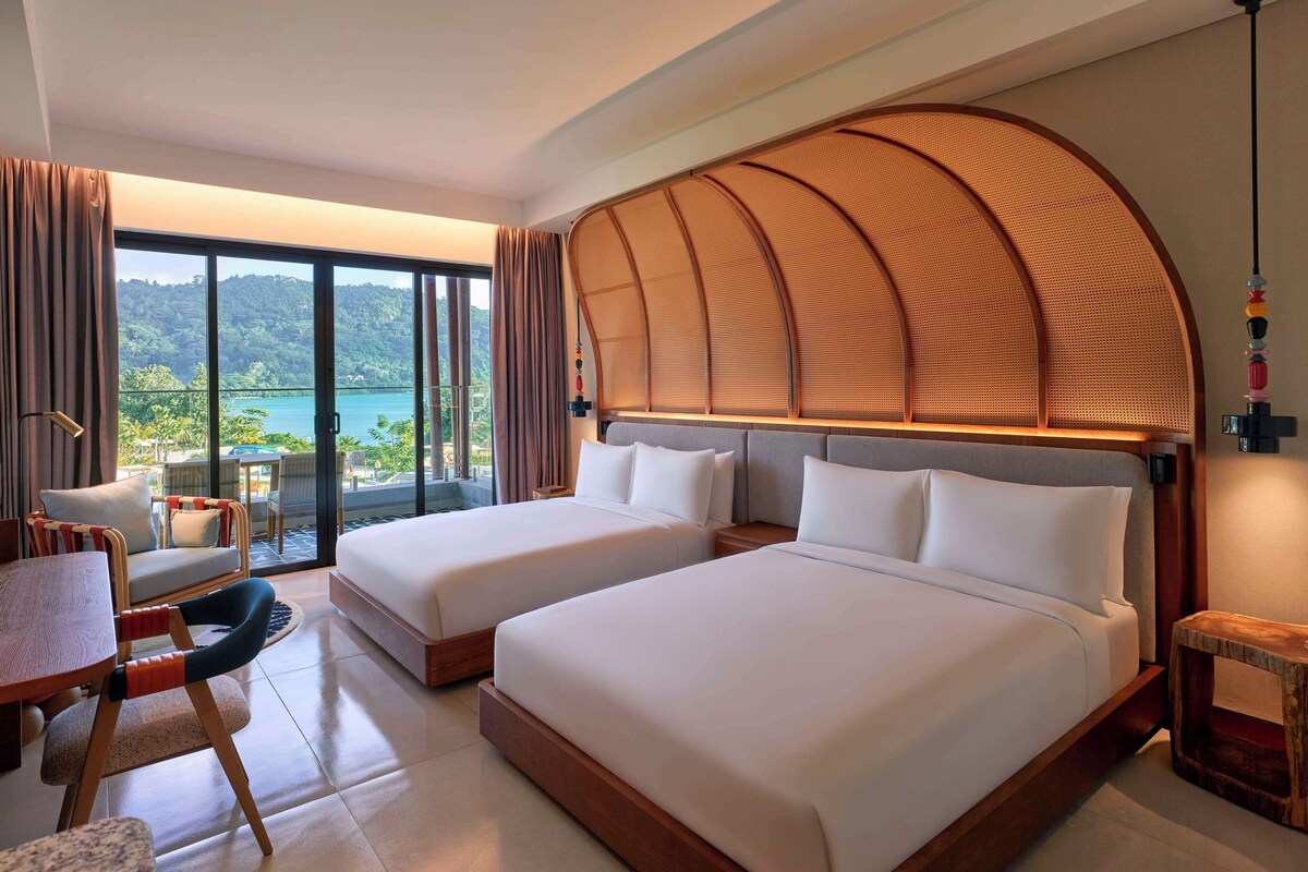 Une chambre d’hôtel avec deux lits, un coin repas et une vue sur un paysage tropical.