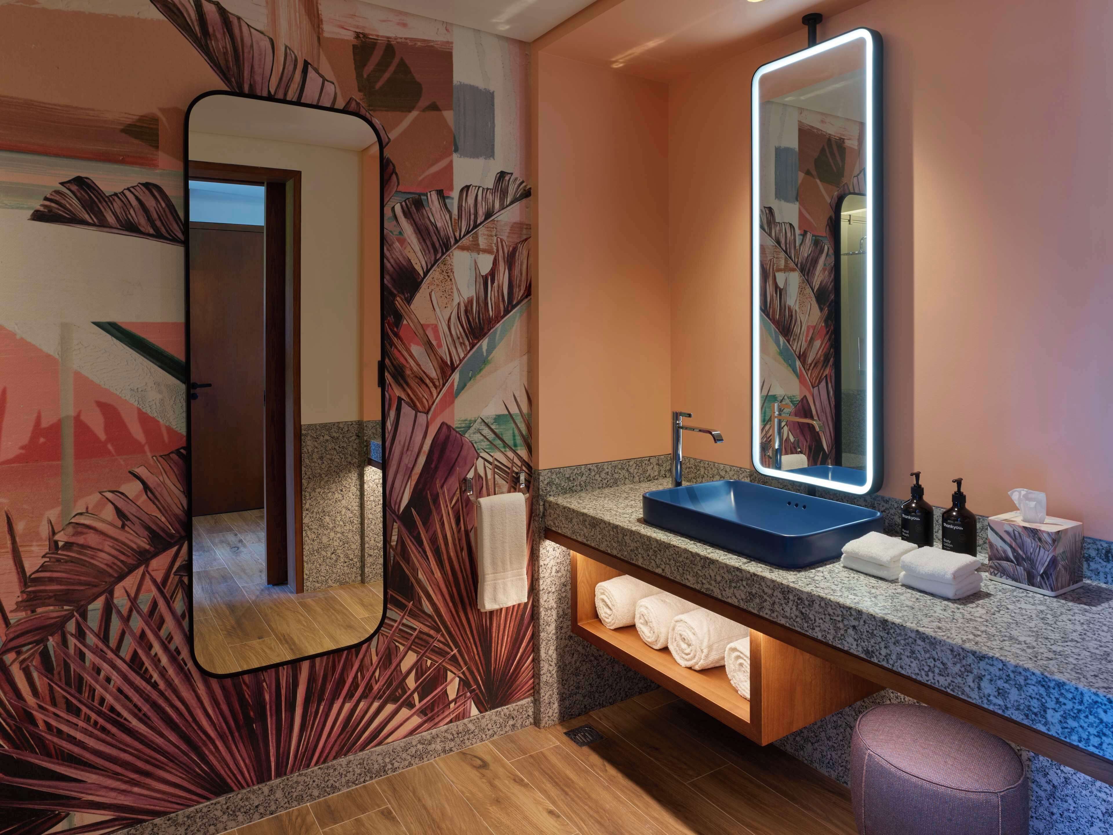 Une salle de bain avec un lavabo bleu, un grand miroir et une étagère à serviettes.