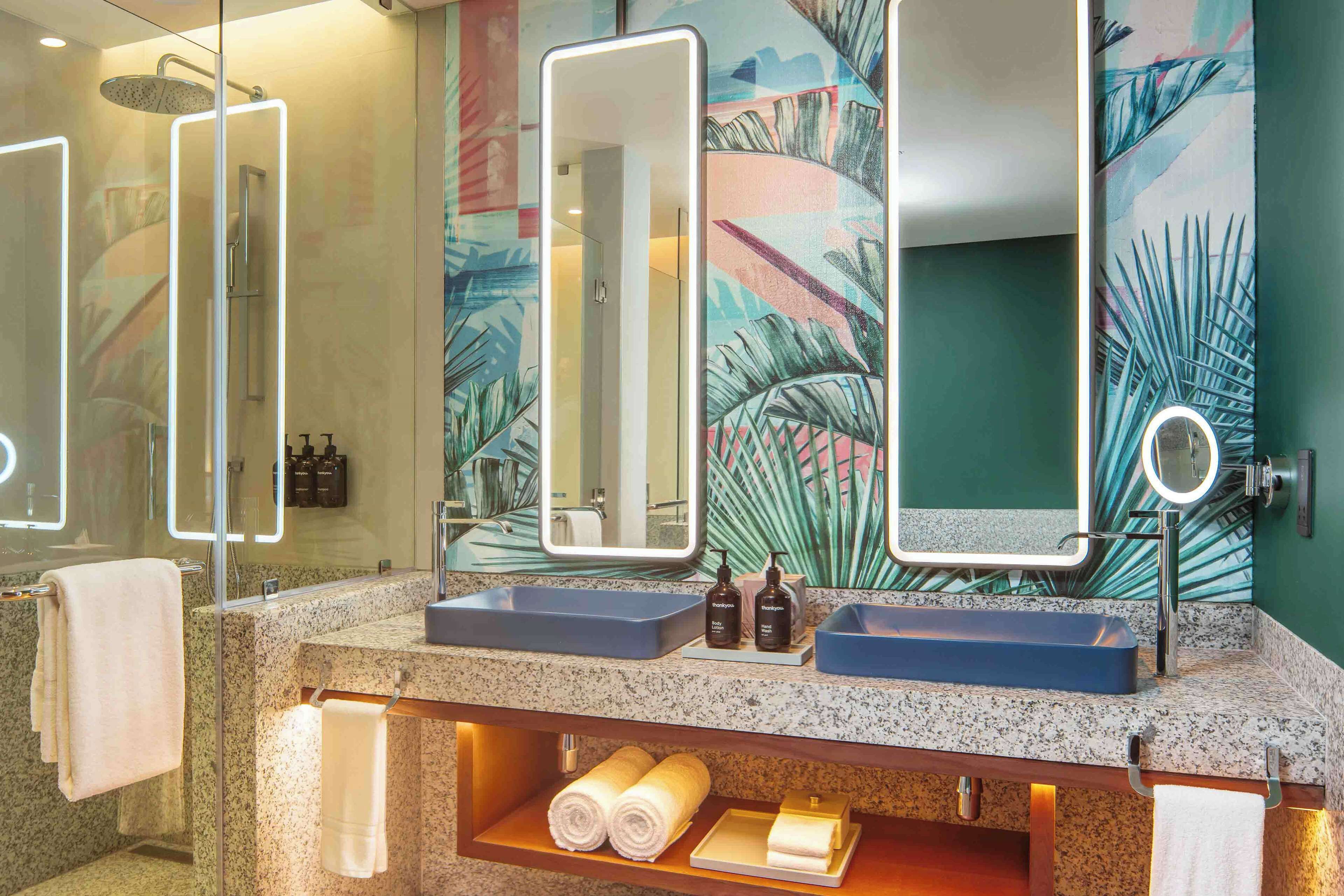 Un baño con encimera de granito, dos lavamanos, un espejo grande y una ducha.
