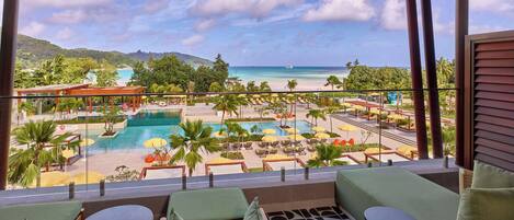 A balcony with a view of a pool, lounge chairs, and a tropical landscape.