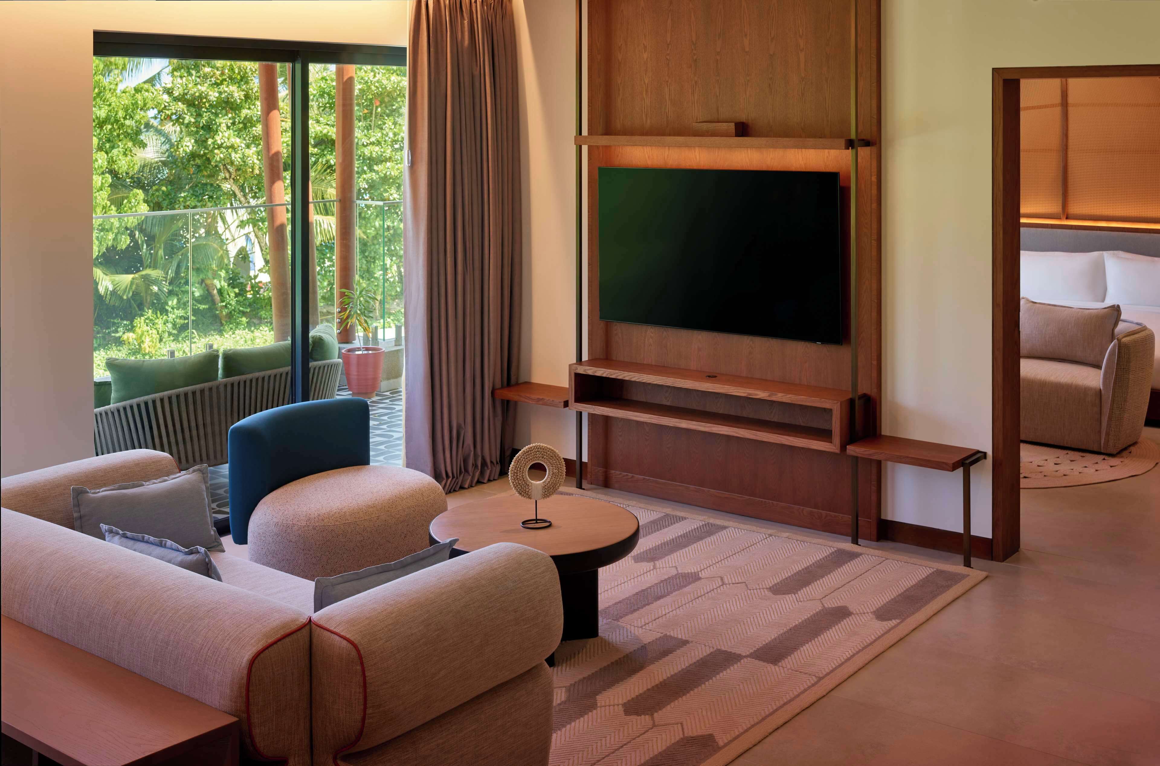 Una sala de estar moderna con un televisor de pantalla plana grande, asientos cómodos, una mesita de centro y vistas a un paisaje verde exuberante.