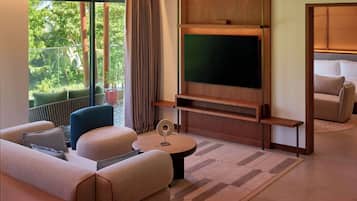 Una sala de estar moderna con un televisor de pantalla plana grande, asientos cómodos, una mesita de centro y vistas a un paisaje verde exuberante.