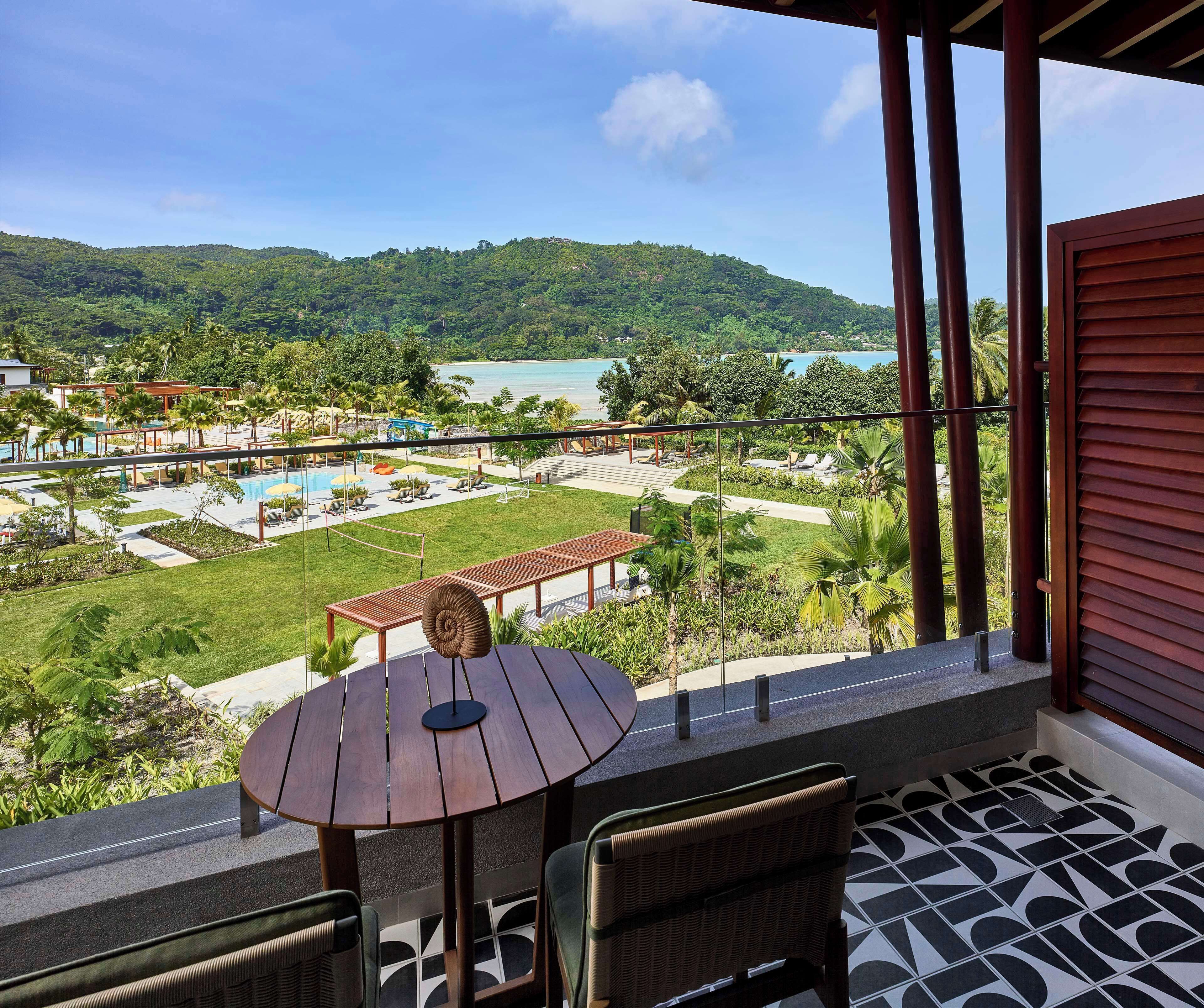 Un balcón con vista a una piscina, zona de estar y exuberante vegetación.
