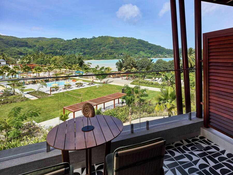 A balcony with a view of a pool, lounge area, and lush greenery.