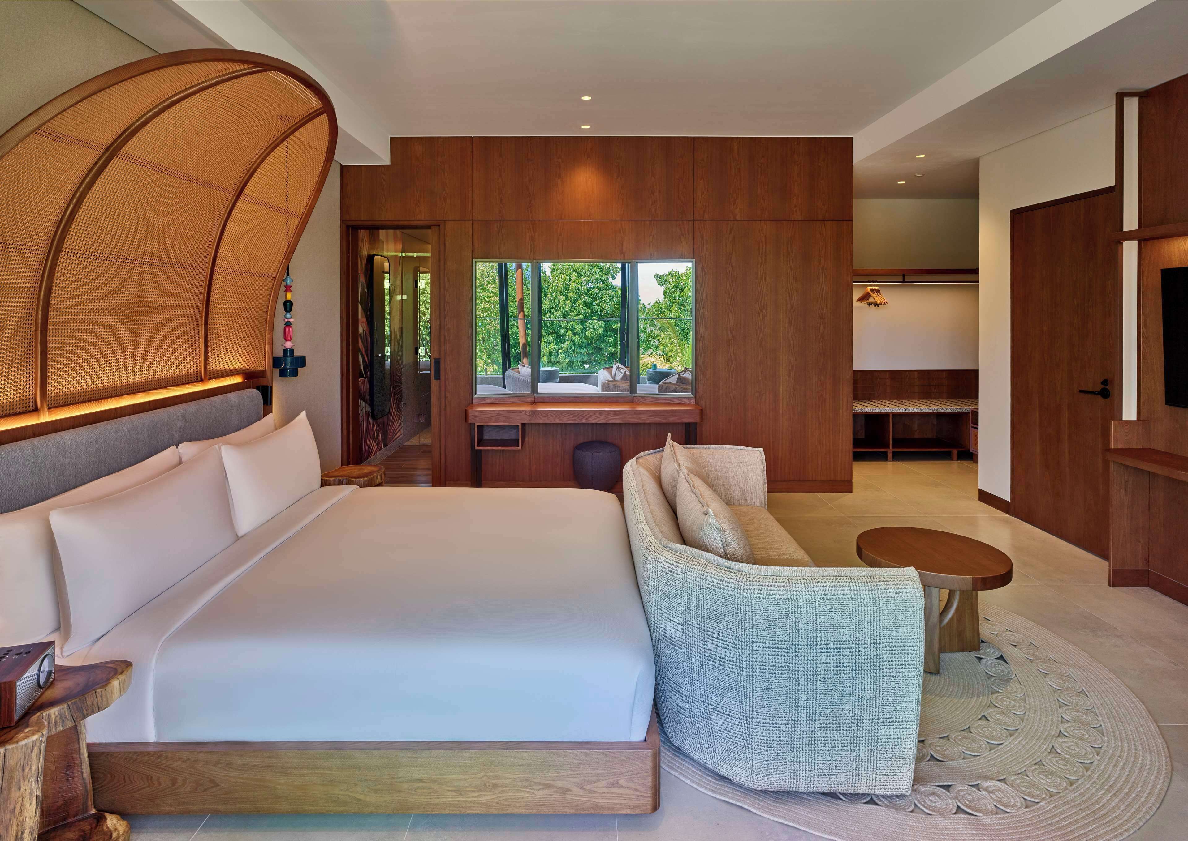 Una habitación de hotel moderna con una cama grande, un sofá, una mesita y un televisor.