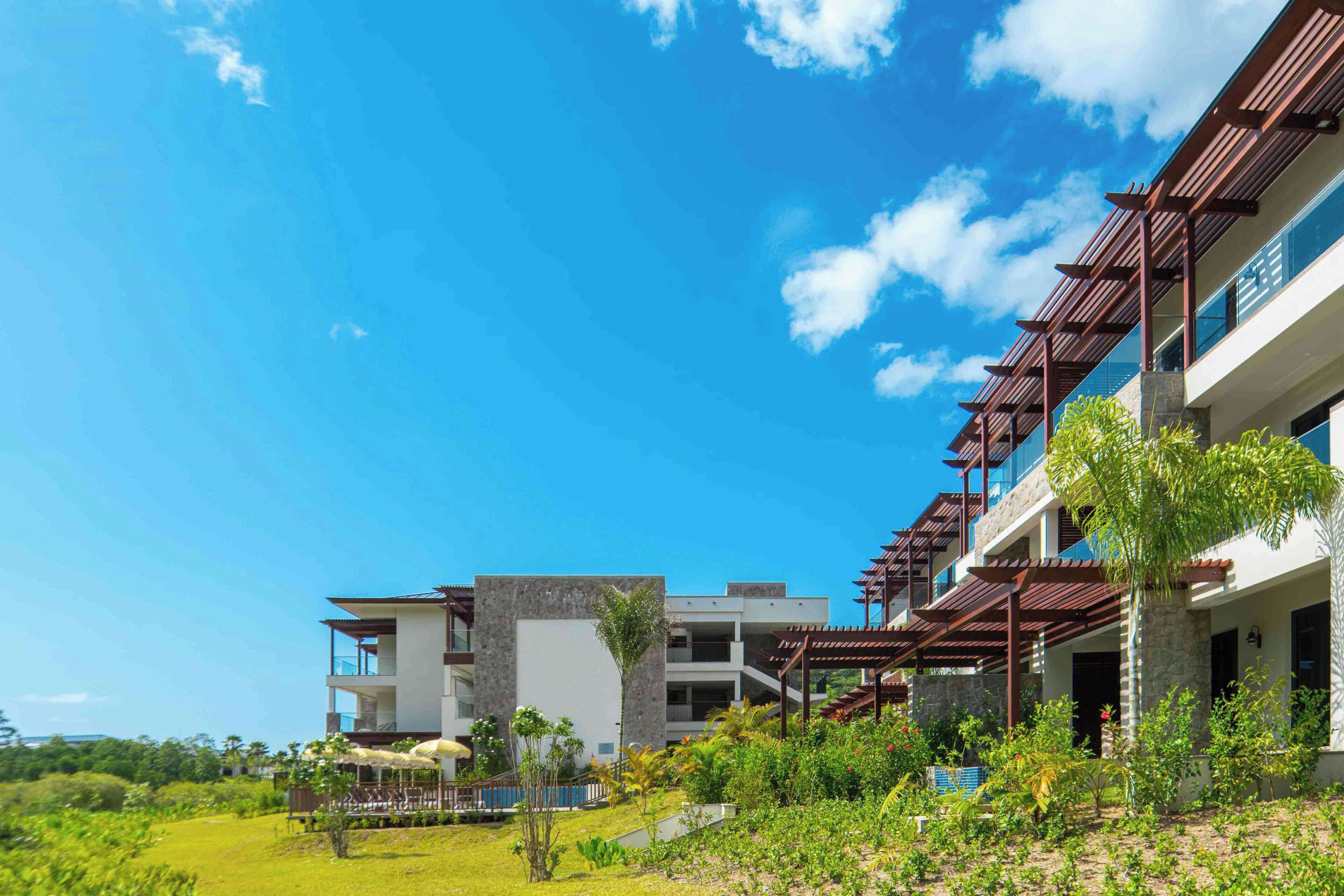 A modern hotel with multiple balconies, a pool area, and lush greenery.