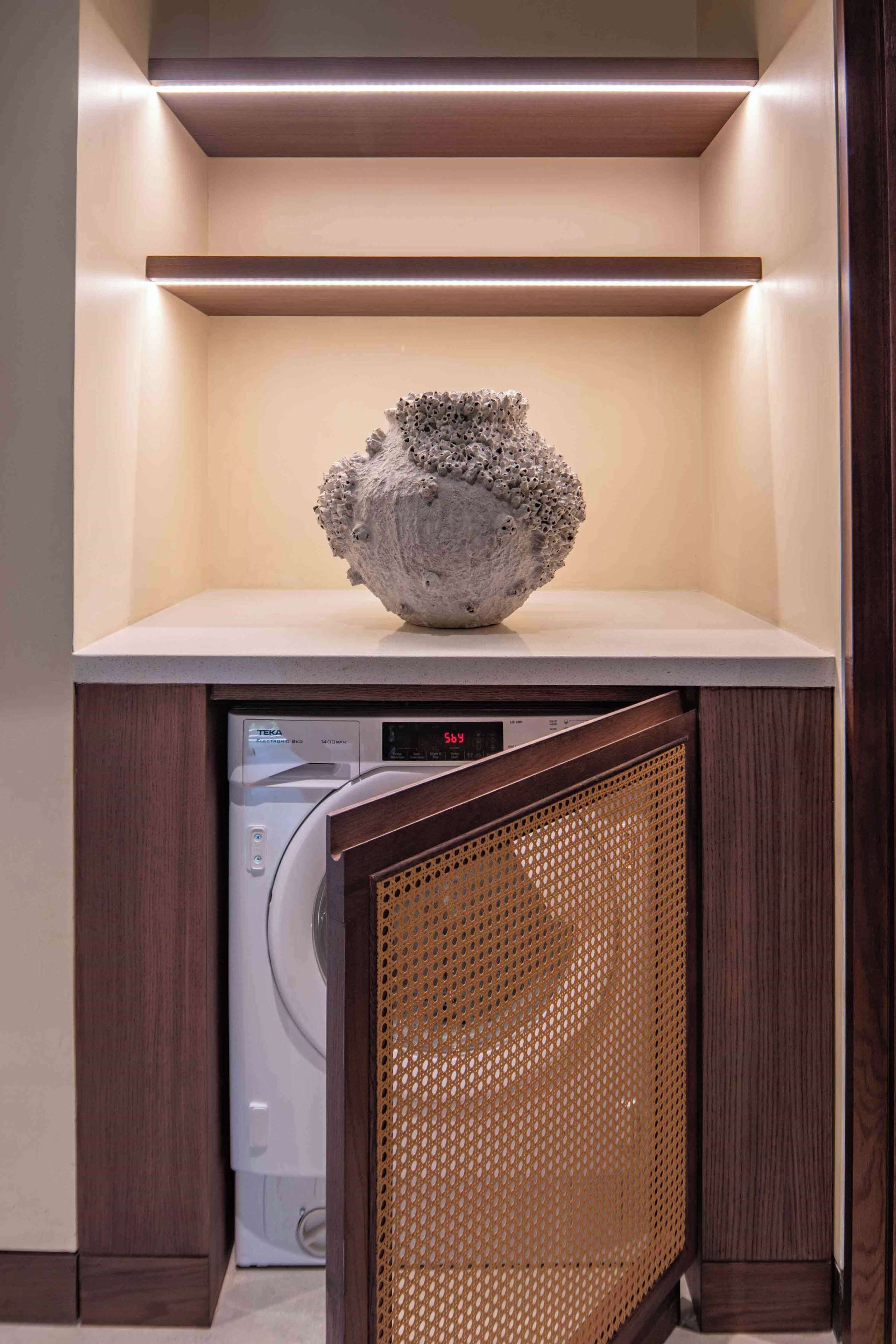 A washing machine under a shelf with a decorative stone.
