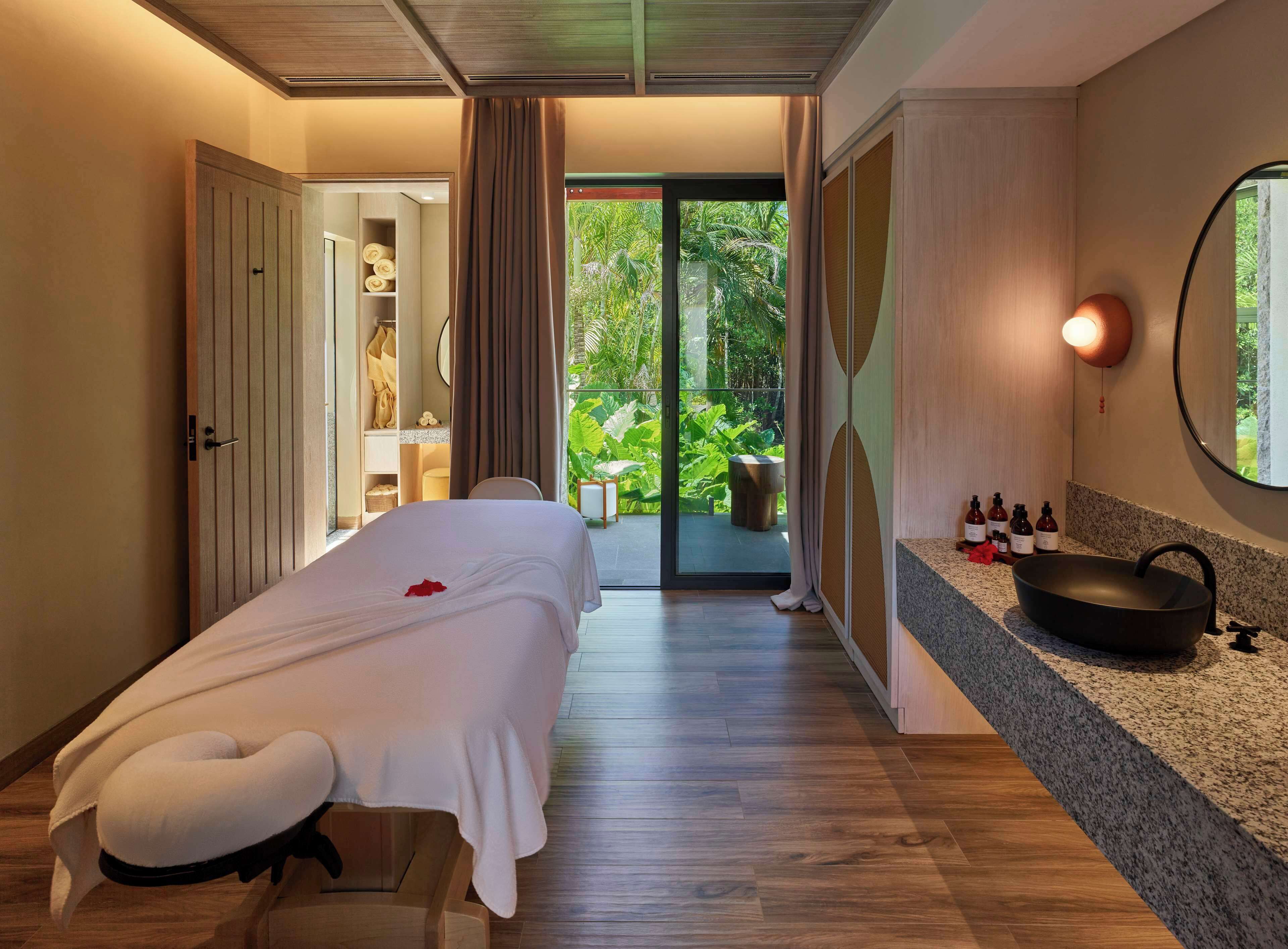 A bedroom with a bed, a bathroom with a sink, and a view of greenery outside.