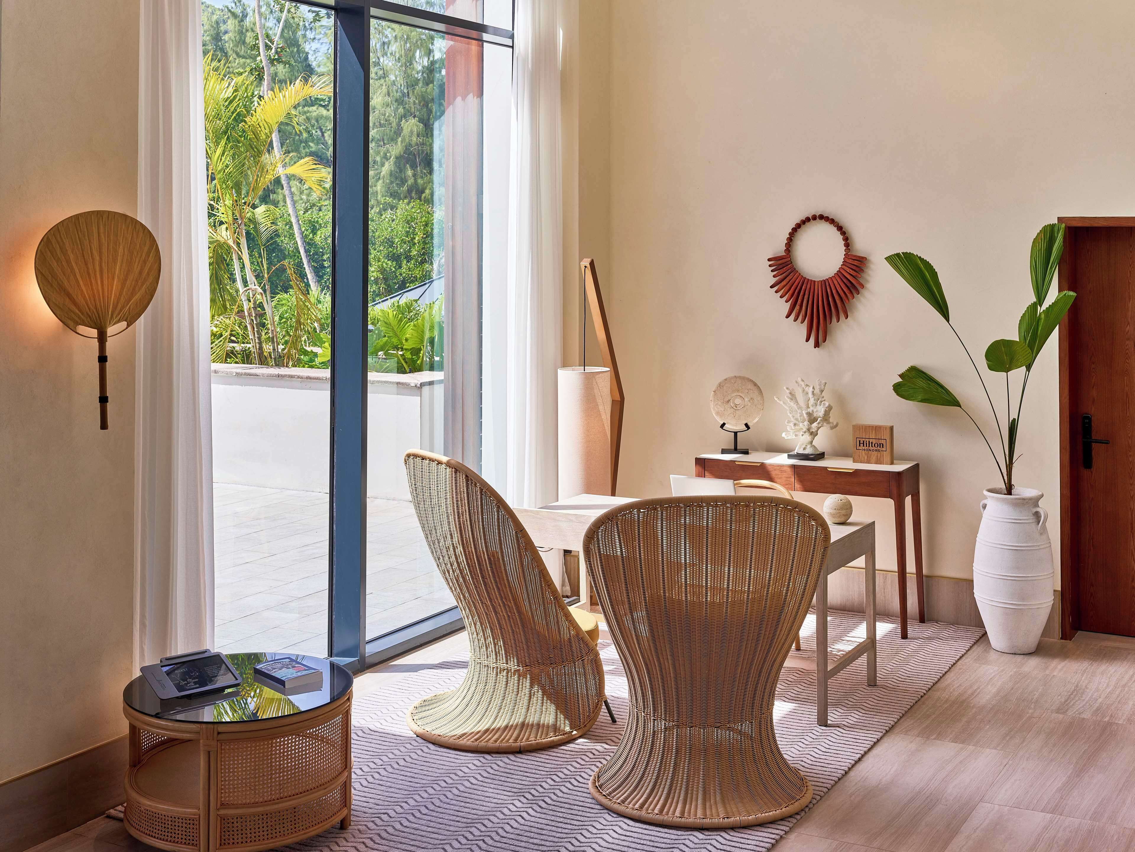 A modern room with wicker furniture, a glass table, and a view of greenery outside.