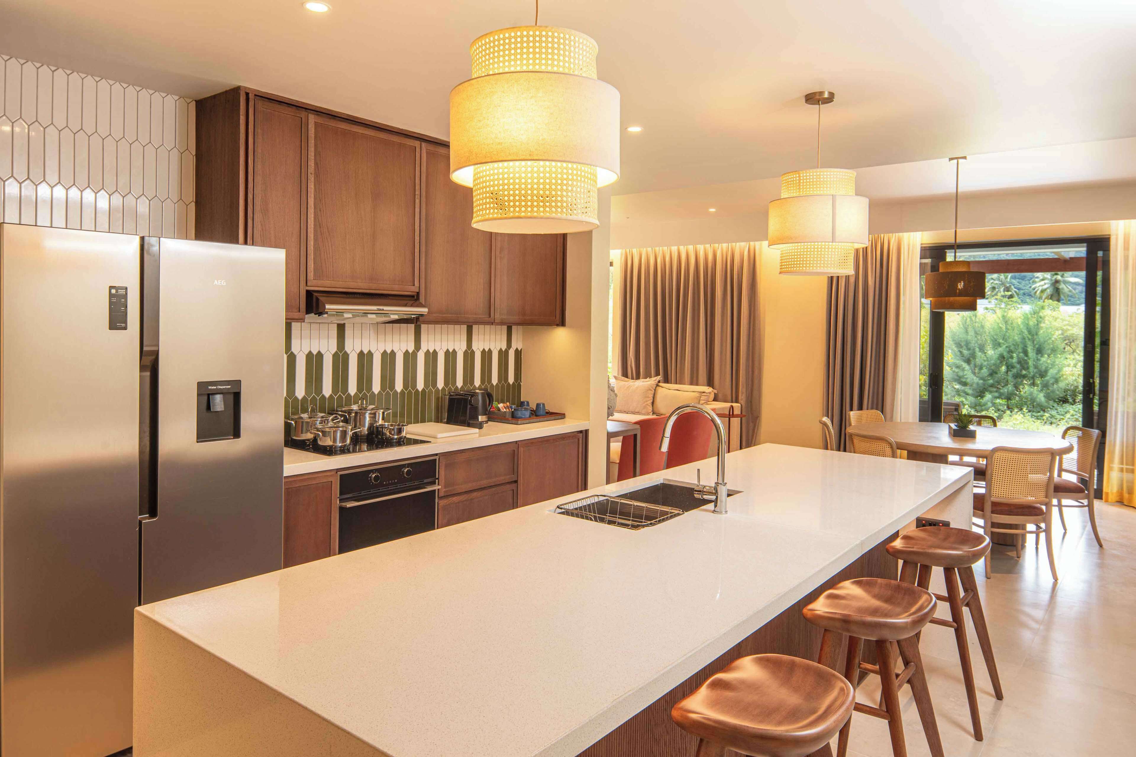 Une cuisine moderne dotée d’un îlot central, d’appareils électroménagers en acier inoxydable et de luminaires suspendus.