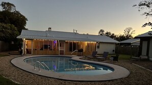 Un patio trasero con piscina, un porche cubierto y mobiliario de exterior.