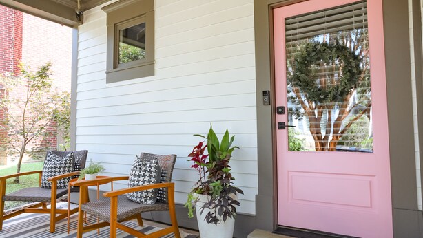 A porch with two wooden chairs, a potted plant, and a pink door with a wreath.