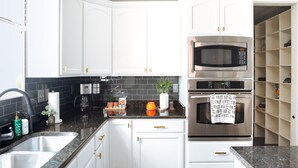 A modern kitchen with white cabinets, a stainless steel microwave, and an oven.