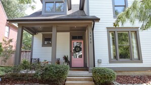 A two-story house with a covered porch, a pink door, and a number '1933' on the wall.