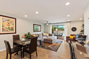 A modern living room with a glass dining table, leather chairs, a grey sofa, and a TV. - 2BR Poolside - 5 minutes to El Paseo - King Bed - Washer/Dryer (Palm Desert)