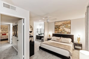 A bedroom with a large bed, a ceiling fan, bedside tables with lamps, and a painting on the wall. - 2BR Poolside - 5 minutes to El Paseo - King Bed - Washer/Dryer (Palm Desert)