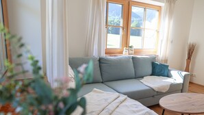 Un soggiorno moderno con un divano grigio, un tavolino rotondo in legno e una finestra con tende.
