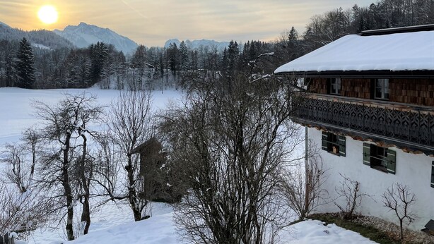 Paesaggio innevato con un edificio dall'architettura tradizionale, circondato da alberi e montagne sullo sfondo.